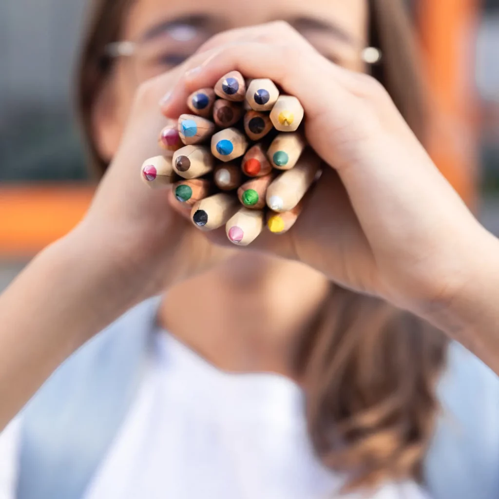 Chancengleichheit in Schulen - Startchancen Programm. Foto: Mädchen hält ein Dutzend Buntstifte in die Kamera (diverse Farben)